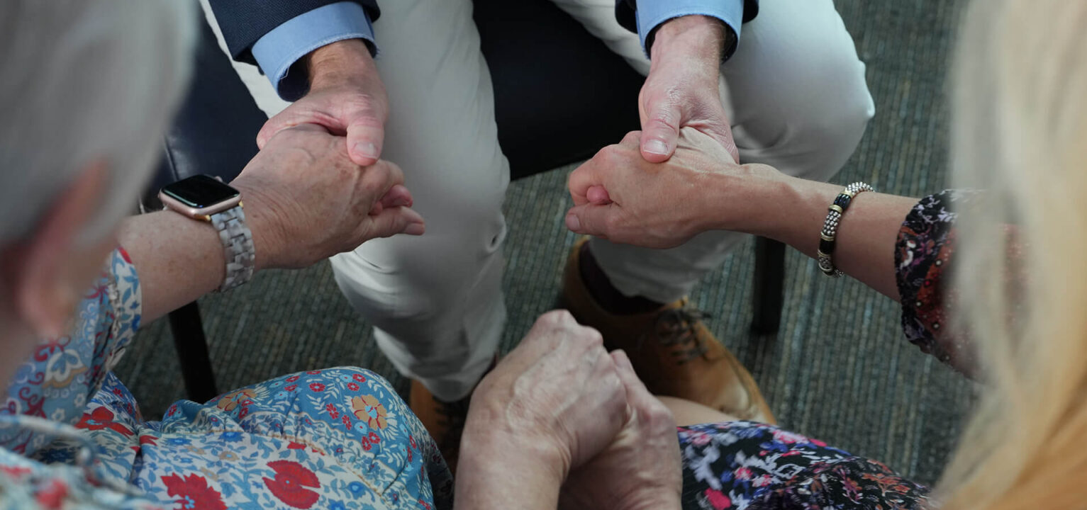 Minister, dementia patient, and daughter holding hands and praying together